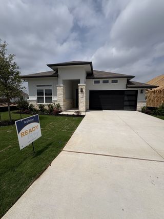 A modern home with stone accents and a sleek garage in Veranda by Brightland Homes (San Antonio, TX).