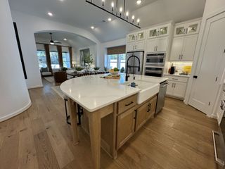 A spacious kitchen with a large island, sleek appliances, and wooden flooring, opening to a cozy living area.