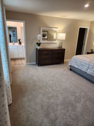 A cozy bedroom with plush carpet, elegant dark wood dresser, and soft lighting leading to a bright, modern bathroom.