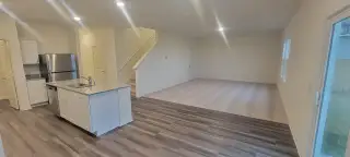 An open-concept living space with modern kitchen, granite counters, and wood flooring. Carpeted stairs in view.