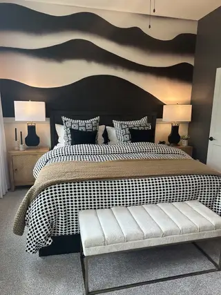 Model Home A modern bedroom featuring bold, artistic wall art, a patterned bedspread, and a cozy upholstered bench.