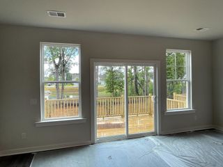 Bright living space with large windows and glass doors opening to a wooden deck, offering a serene view of greenery.