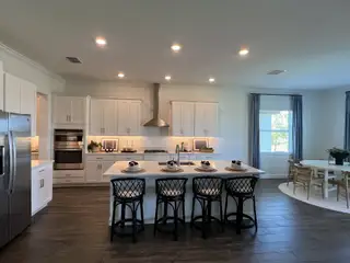 A modern kitchen with sleek white cabinets, an island with seating, stainless steel appliances, and elegant lighting.