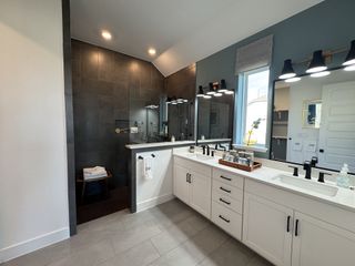 A spacious master bathroom with dual vanities, black fixtures, and a luxurious walk-in shower with dark tile.