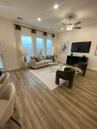 Model Home A cozy living room with warm wood flooring, large windows, and a ceiling fan, perfect for relaxation.