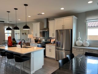 A contemporary kitchen featuring sleek white cabinets, a central island with pendant lighting, and a modern stainless steel fridge.