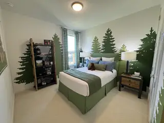 A charming nature-inspired bedroom with tree wall art, green accents, and cozy bedding, ideal for a child’s retreat.