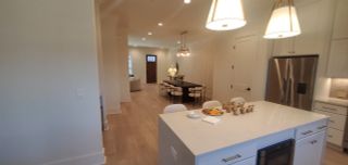 A modern open-concept kitchen and dining area with sleek lighting, an island, and warm wood flooring.