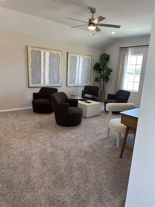 A cozy living area with plush chairs, modern art, and a chic ceiling fan, perfect for relaxation and gathering.