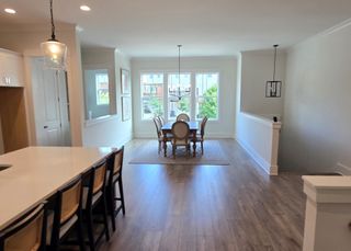 Model Home An elegant dining room with natural light, wood flooring, and a modern chandelier, open to an island kitchen.