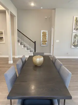 A modern dining area with a sleek table, gray chairs, and stylish artwork, enhanced by contemporary decor and warm lighting.
