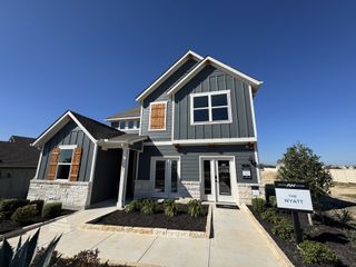 Street view A charming two-story blue home with wooden shutters in Cannon Ranch 40s by Ashton Woods (Dripping Springs, TX).