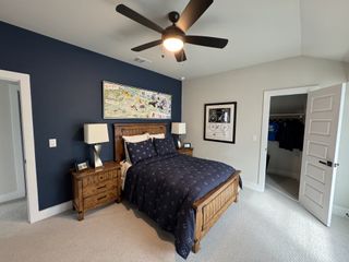 A cozy bedroom with a navy accent wall, wooden furniture, and a ceiling fan, offering a walk-in closet space.