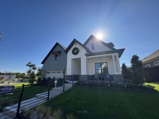 Model Home A bright and inviting home with a covered porch, elegant landscaping, and a welcoming pathway in Headwaters by David Weekley Homes (Dripping Springs, TX).