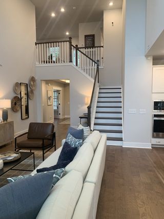 A spacious living room with a cozy sectional, leather chair, and elegant staircase, accented by modern decor and warm lighting.