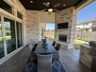 A cozy outdoor patio with stone walls, a ceiling fan, and a fireplace, featuring a sleek dining area for entertaining.