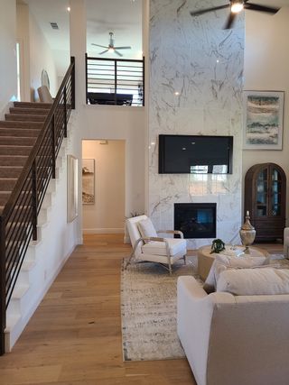 A modern living room with high ceilings, marble fireplace, cozy seating, and an elegant staircase.