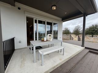 Outdoor patio area with a table and bench seating, leading to a wooden deck and overlooking a landscaped yard.