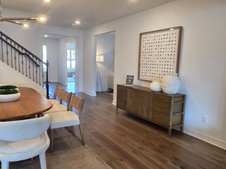 A contemporary dining area with a sleek wood table, elegant staircase, and modern decor, featuring neutral tones and stylish lighting.